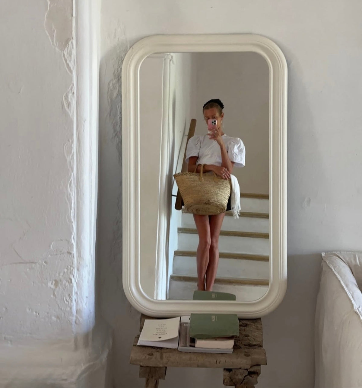 Person holding a woven bag in front of a large mirror on a wooden stand.